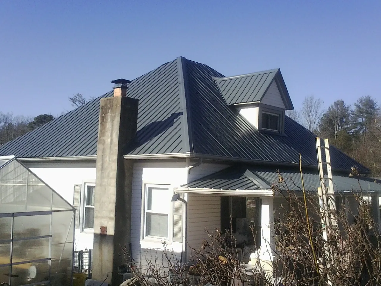 Dark blue standing seam metal roof on a white farmhouse with dormer — Slate & Tile Roof Repair by Roofing Brothers in Stonyford