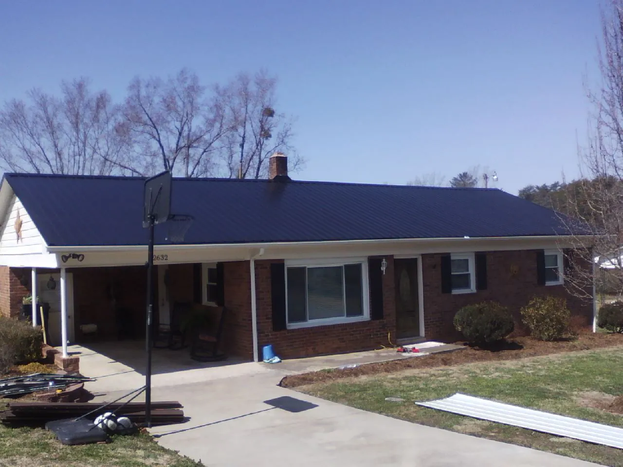 Finished dark blue metal roof on a brick ranch with a carport in Stonyford