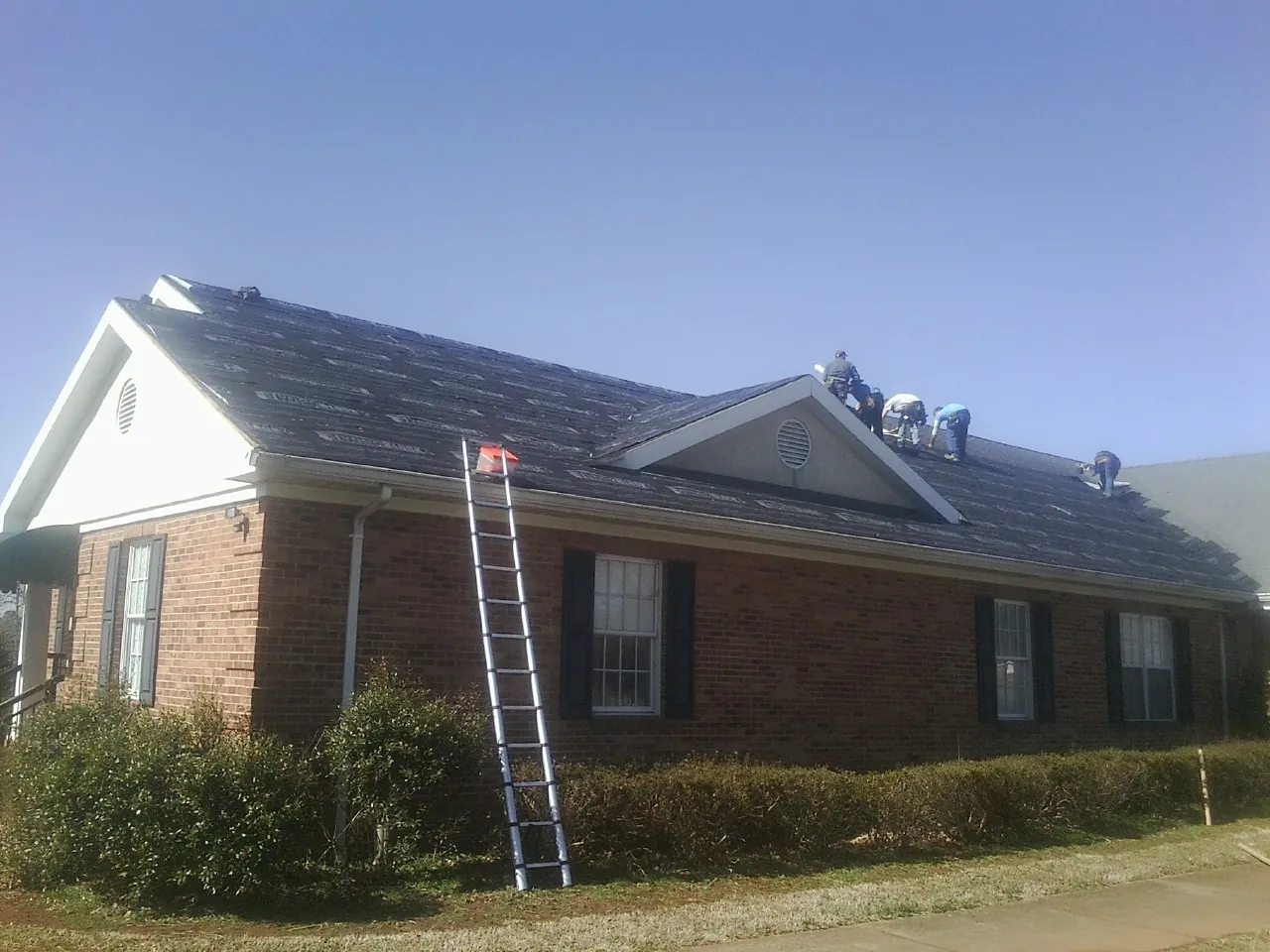 Crew tearing shingles off a brick ranch roof with a ladder set — Metal Roof Repair work by our crew in Stonyford