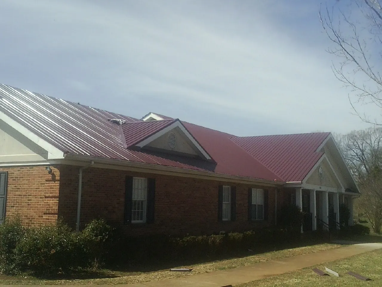 Red metal roof with gabled entries on a long brick building, from a Hail Damage Roof Repair job in Stonyford