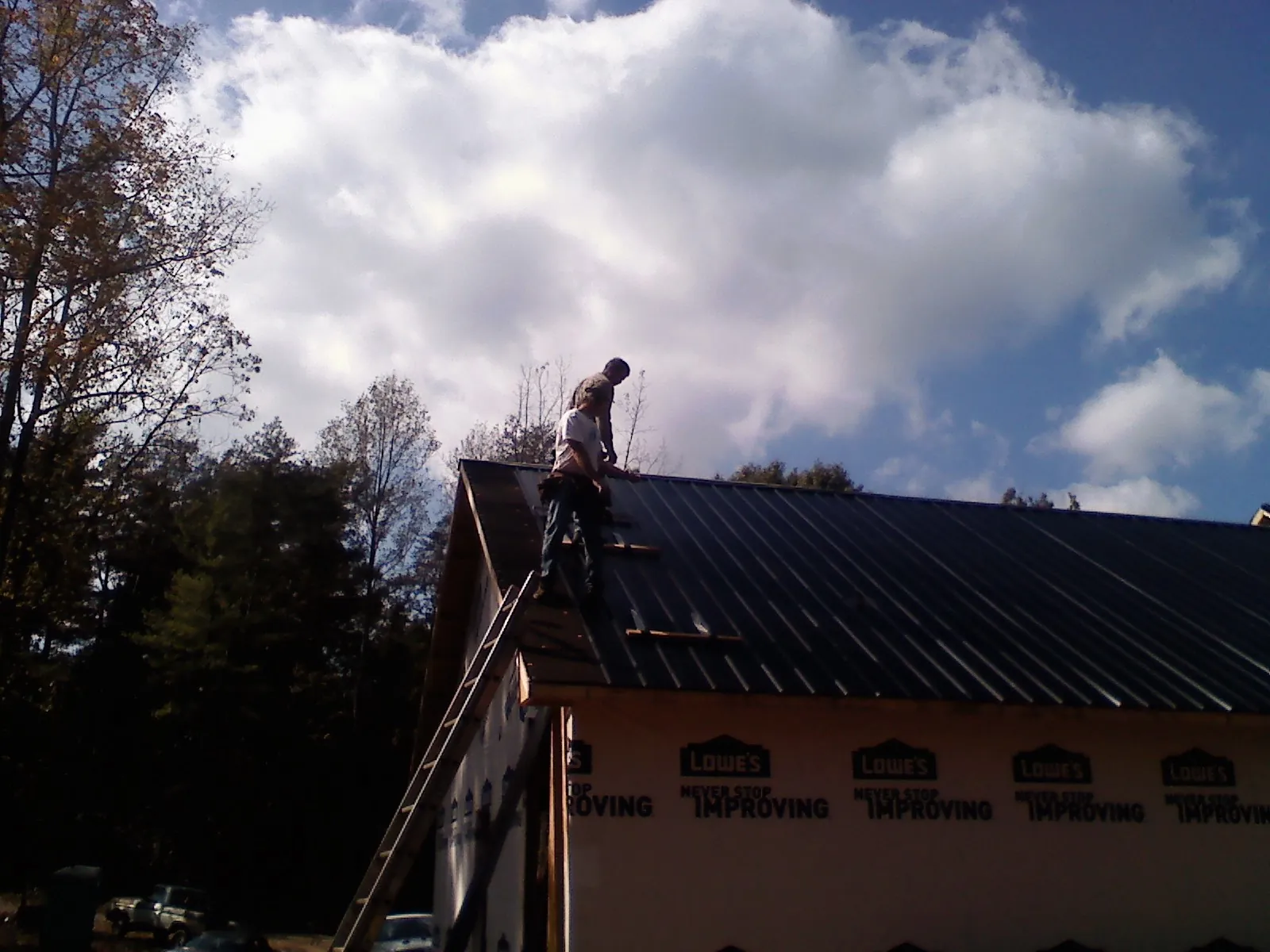 Roofer fastening dark metal panels high against a cloudy sky, from a Roof Inspection job in Stonyford