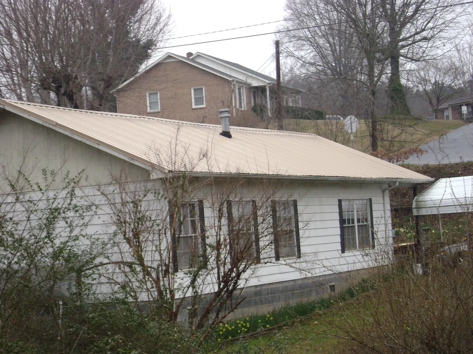 Tan metal roof on a white sided house set into a hillside — Commercial Roofing by Roofing Brothers in Stonyford